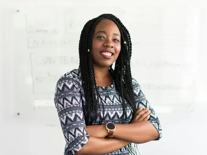 Smiling woman with braided hair standing confidently with folded arms in front of a whiteboard in office